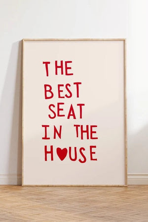 Plakat med rød tekst “The Best Seat in the House” og hjerte – humoristisk vægkunst til badeværelse eller gæstetoilet, indrammet og opstillet i moderne interiør.