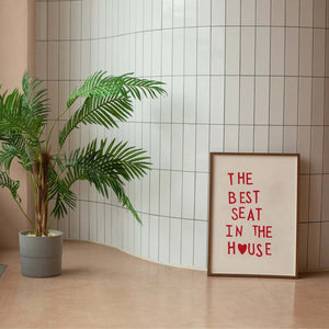 Plakat med rød tekst “The Best Seat in the House” og hjerte – humoristisk vægkunst til badeværelse eller gæstetoilet, indrammet og opstillet i moderne interiør.