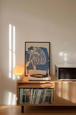 Kunstnerisk plakat med siddende figur i blå striber og bløde former på lys baggrund