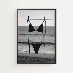 Sort-hvid strandplakat med sort bikini hængende foran havet.