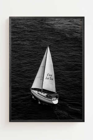 Sort-hvid plakat med sejlbåd på åbent hav og teksten C'est La Vie på sejlet.