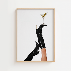 Denne fashion-inspirerede cocktailplakat fanger det perfekte øjeblik — sorte lakstøvler løftet mod himlen med et martiniglas balanceret på spidsen.