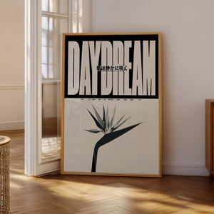 Daydream plakat med stor beige typografi, japansk tekst og stiliseret blomst i egetræsramme på gulv ved vindue