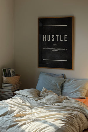 Hustle plakat med sort baggrund og hvid typografi og definition i egetræsramme over seng