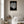 Hvid koral plakat i sort ramme over reol i moderne stue