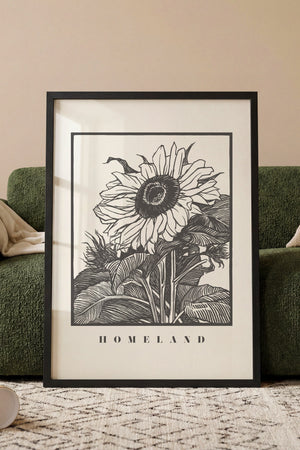 Solsikke Homeland plakat med grafisk blomstermotiv i sort hvid i egetræsramme ved sofa