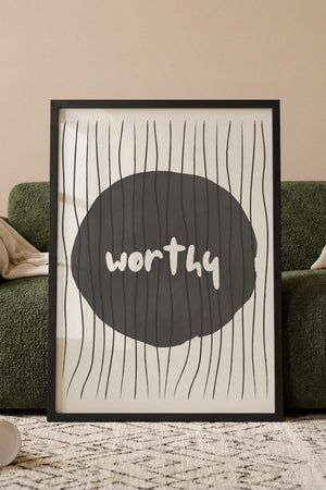 Worthy cirkel plakat med tekst i hvidt på mørk cirkel og stribede streger i egetræsramme ved sofa